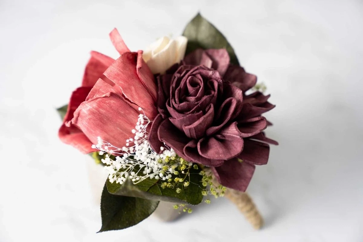 Close view of a groom's boutonniere made with burgundy wood flowers and baby's breath