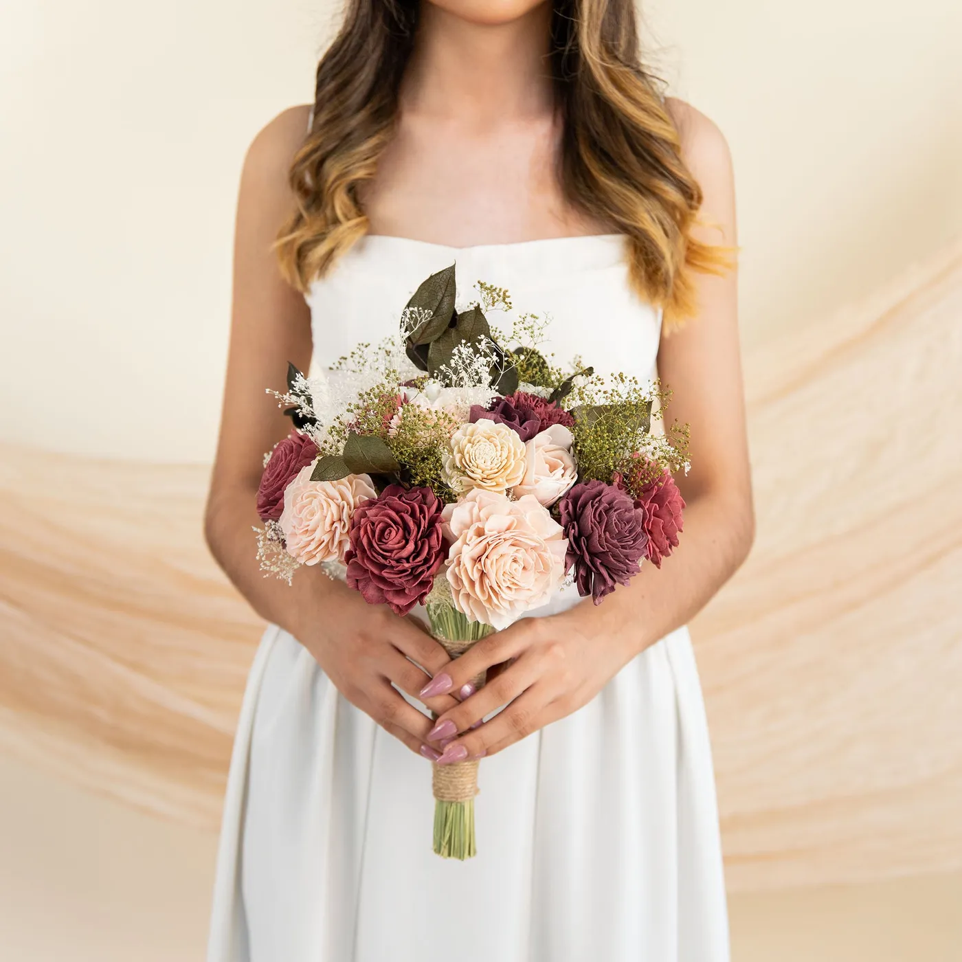 Bride in a white dress holding the Love Story bridal bouquet of pink, burgundy and cream wood flowers
