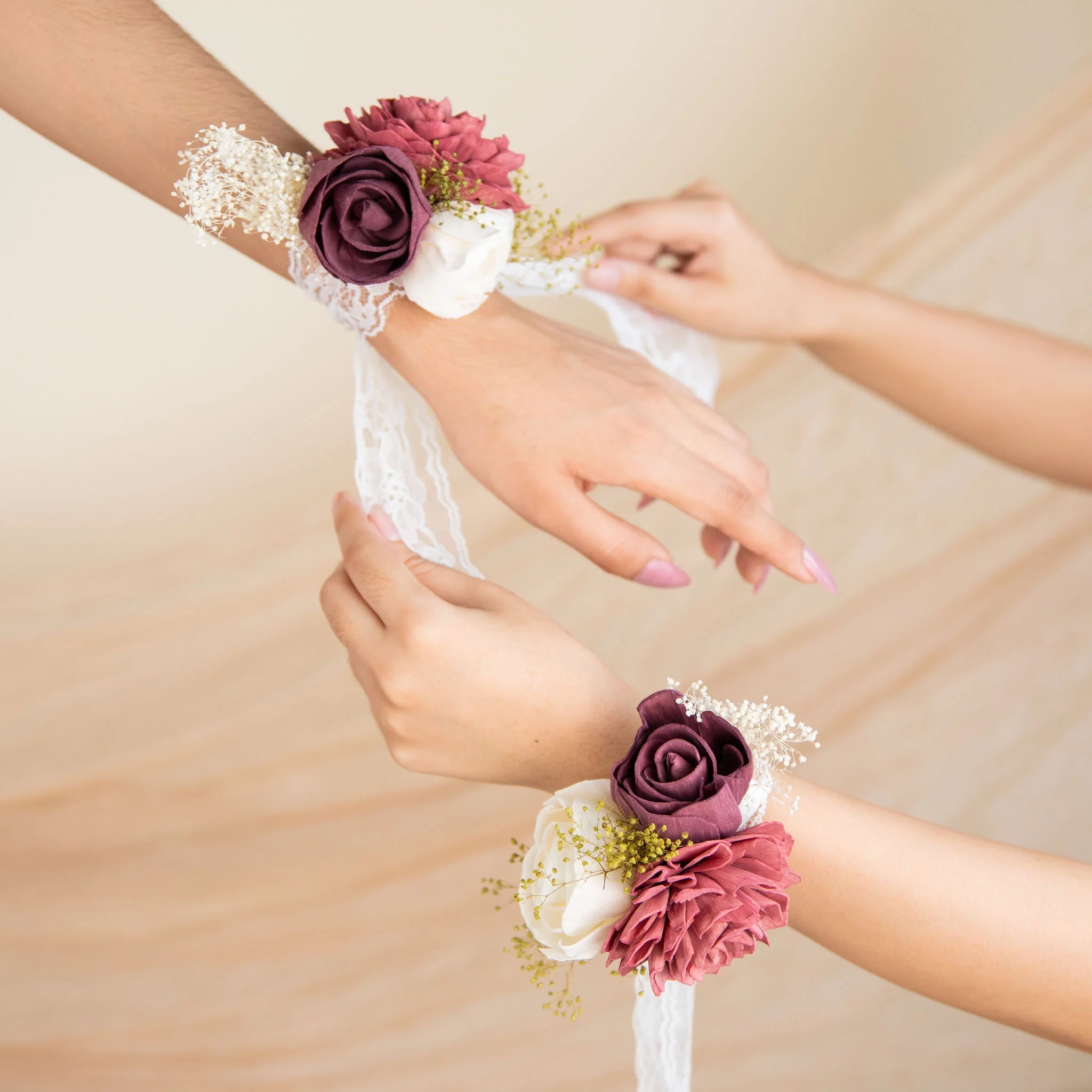 Hands fastening a Love Story wrist corsage of burgundy and cream wood flowers